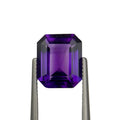Amethyst gemstone held between tweezers on a white background