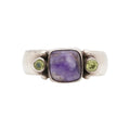 Silver ring with a charoite gemstone and two green gemstones on a white background